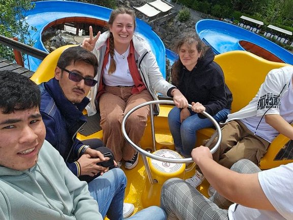 Das Bild zeigt mehrere Menschen in einem Fahrgeschäft mit Lenkrad in der Mitte.