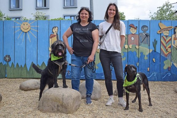 Ein Gruppenbild von zwei Frauen und zwei Hunden. Links Begleithund Paula mit ihrer Hundeführerin Rebecca Gräfenstein und rechts Hund Bolle mit Hundeführerin Katharina Brekken.  