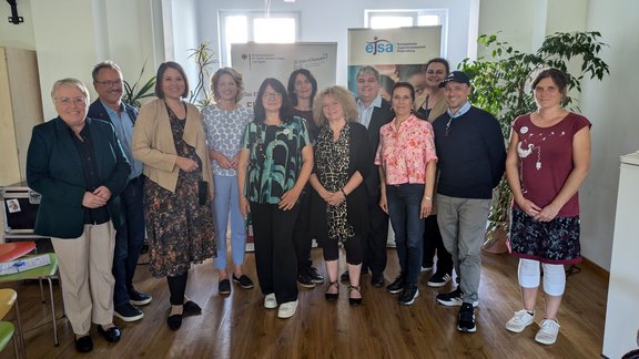 Das Bild zeigt ein Gruppenfoto mit 12 Personen, die in die Kamera schauen und lächeln.   