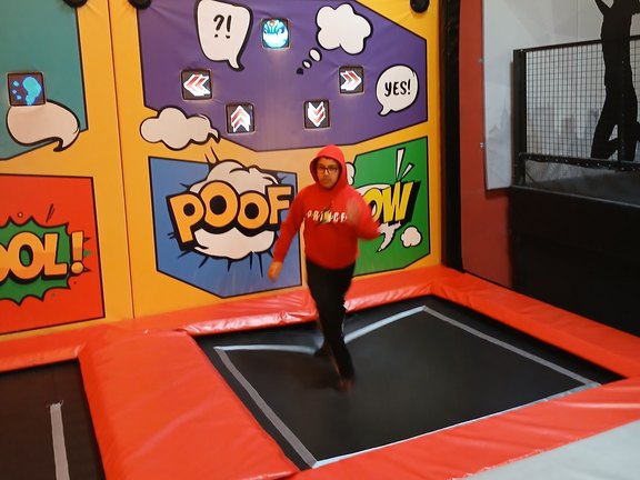 Corona Speer, OGS Undorf Ein Schüler in Pullover springt auf einem Trampolin vor buntem Hintergrund.