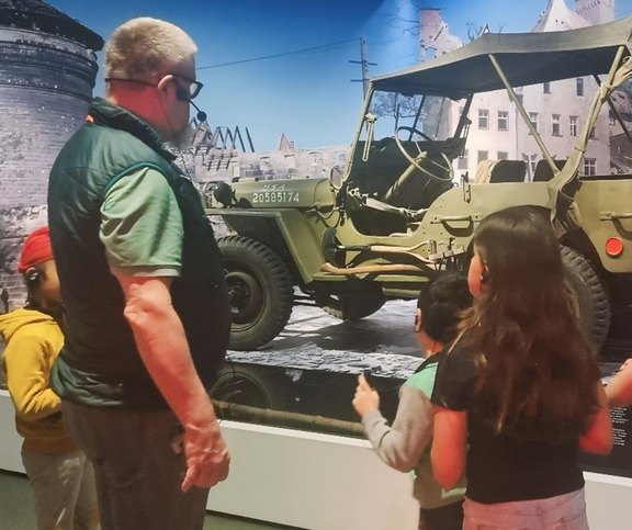 Das Bild zeigt Kinder mit einem Mann vor einem Fahrzeug.  